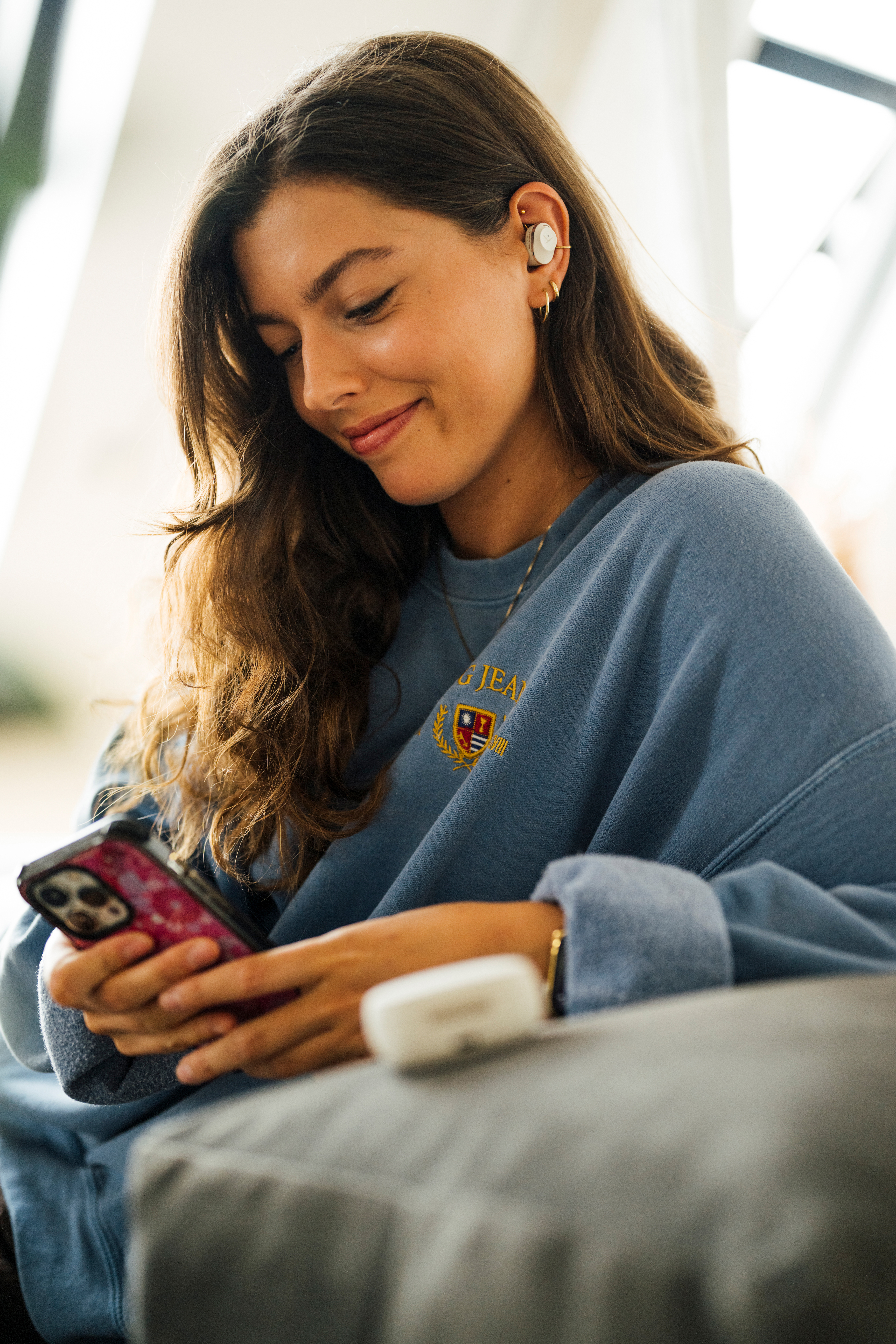 Frau mit Ohrhörern und blauem Pullover, benutzt ein Handy.