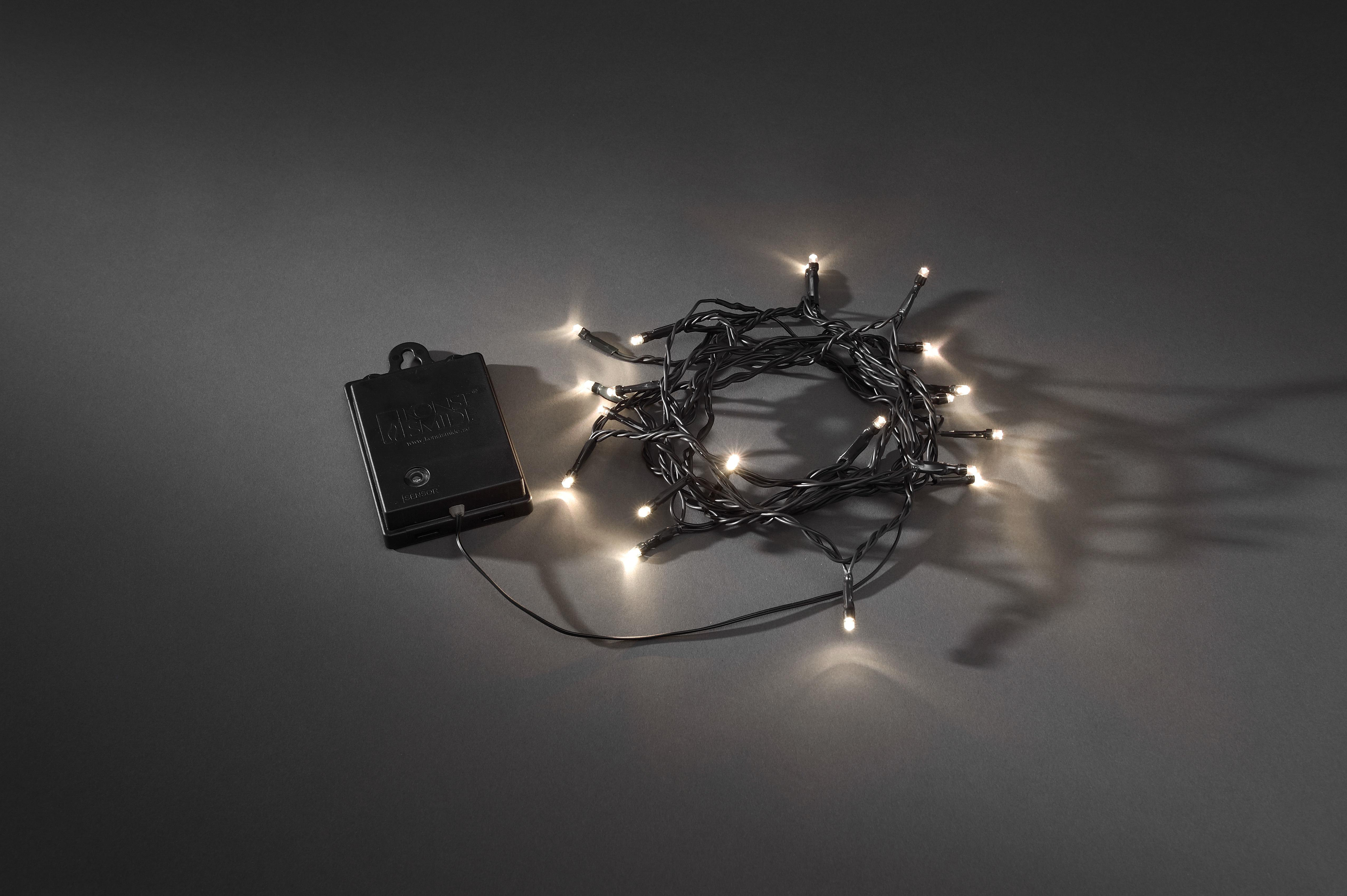 Eine Lichterkette mit weißen Lichtern liegt auf grauer Oberfläche. Akku links.