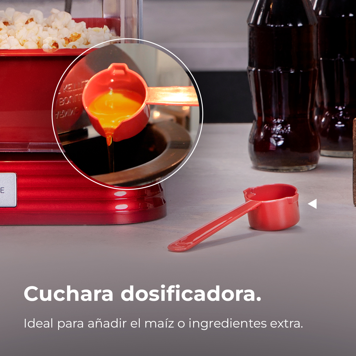 Una máquina de palomitas roja con una cuchara de aceite vertiéndose en ella, con dos botellas de refresco en el fondo.