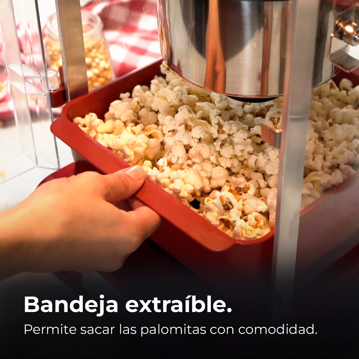 Una máquina de palomitas roja con palomitas reventadas. Una mano sostiene el recipiente.