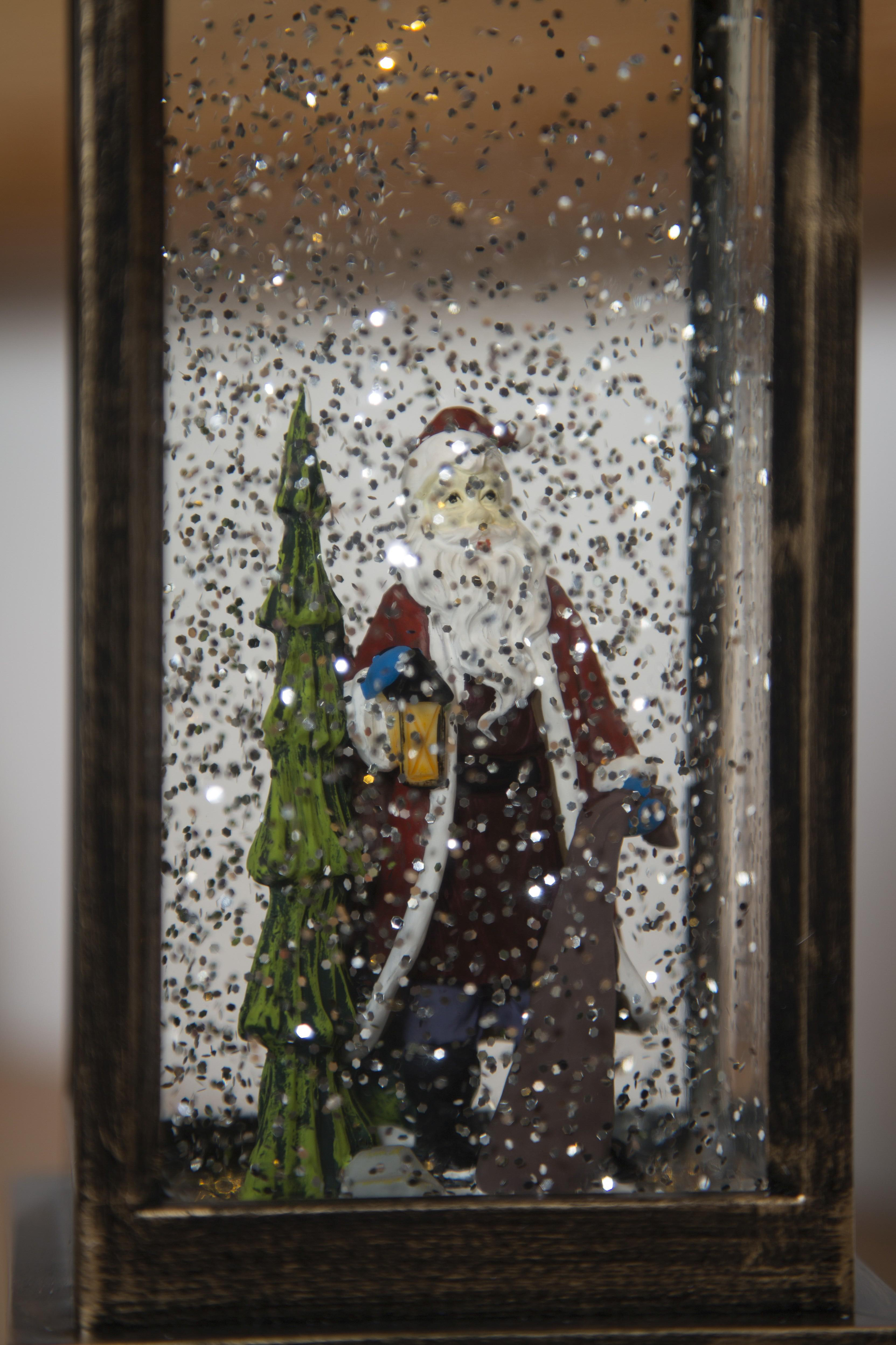 Schneekugel mit Weihnachtsmann und Weihnachtsbaum. Glitzer schwebt im Inneren des Glases.