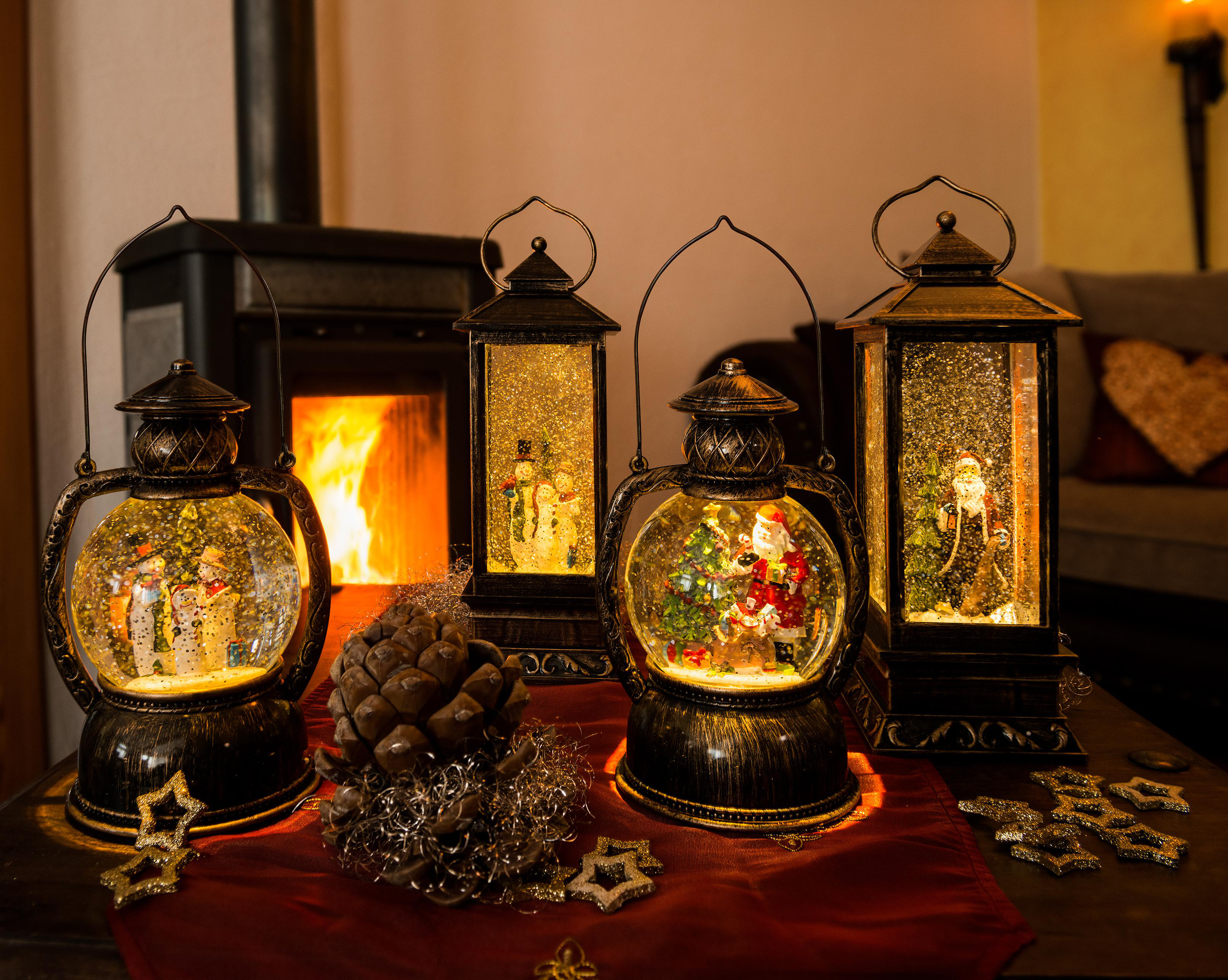 Vier Weihnachtsschneekugeln auf einem Tisch, Kamin im Hintergrund.