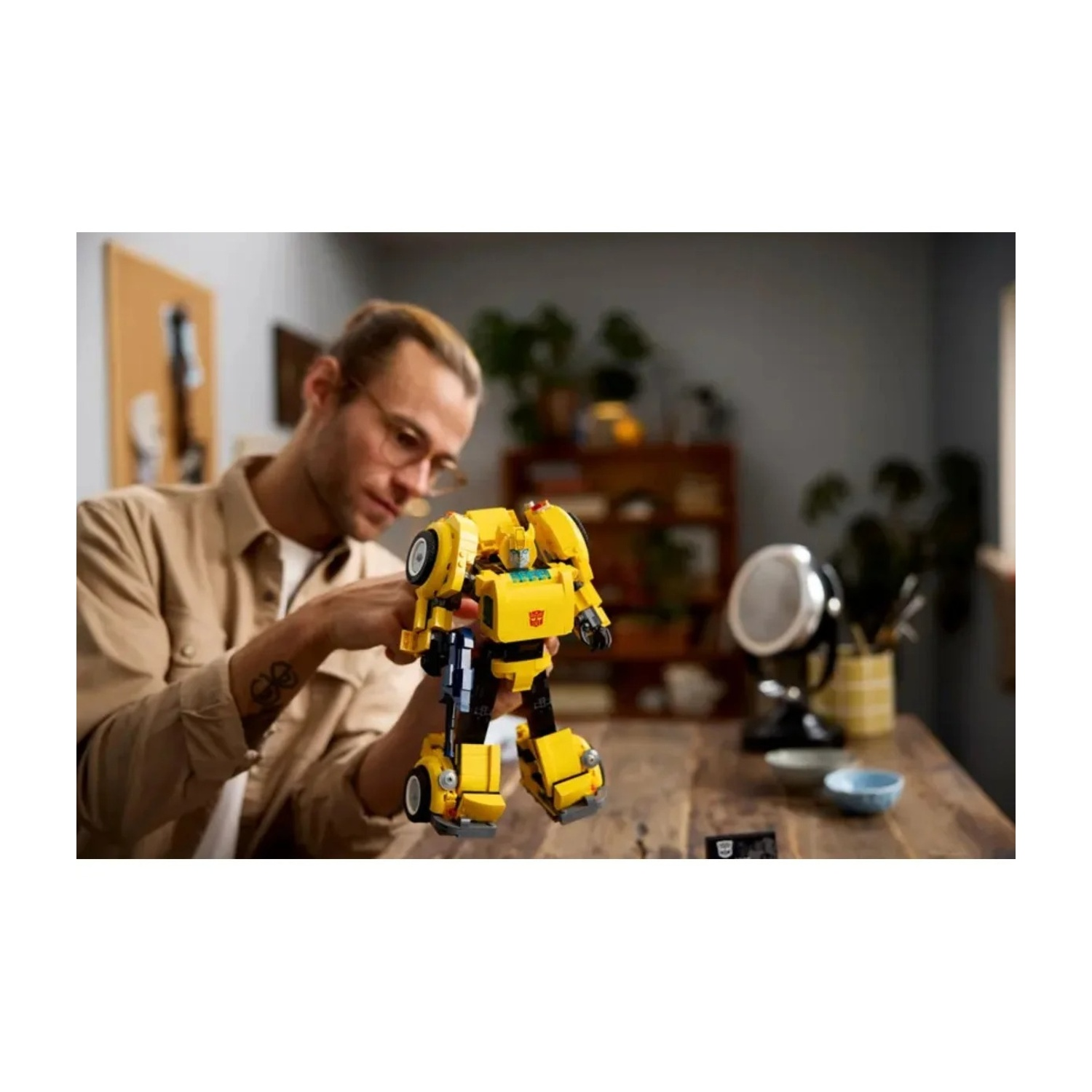 Un uomo guarda una figura Lego Bumblebee Transformer su un tavolo di legno.