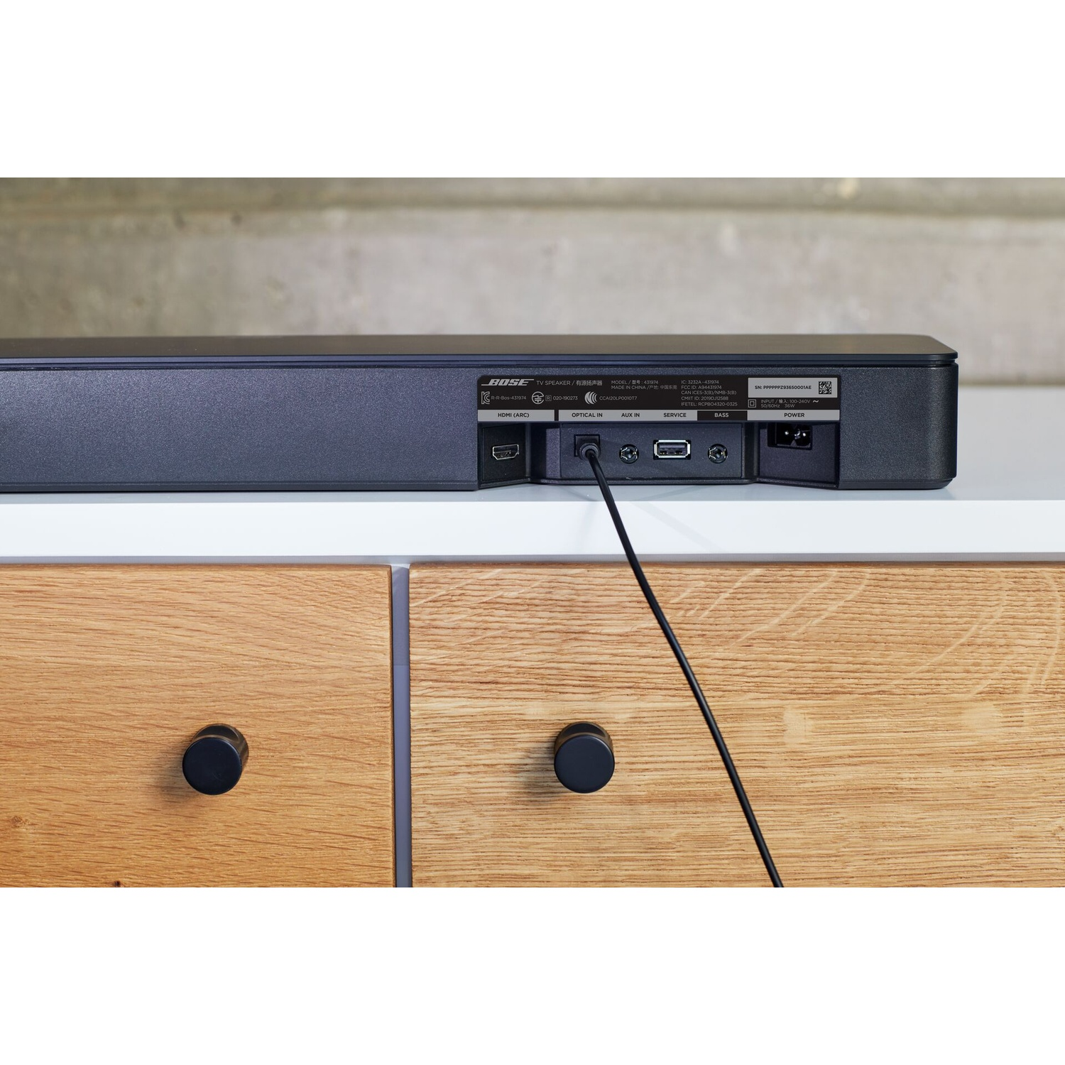 Retro di una soundbar nera con porte e superficie bianca, con cavo collegato.