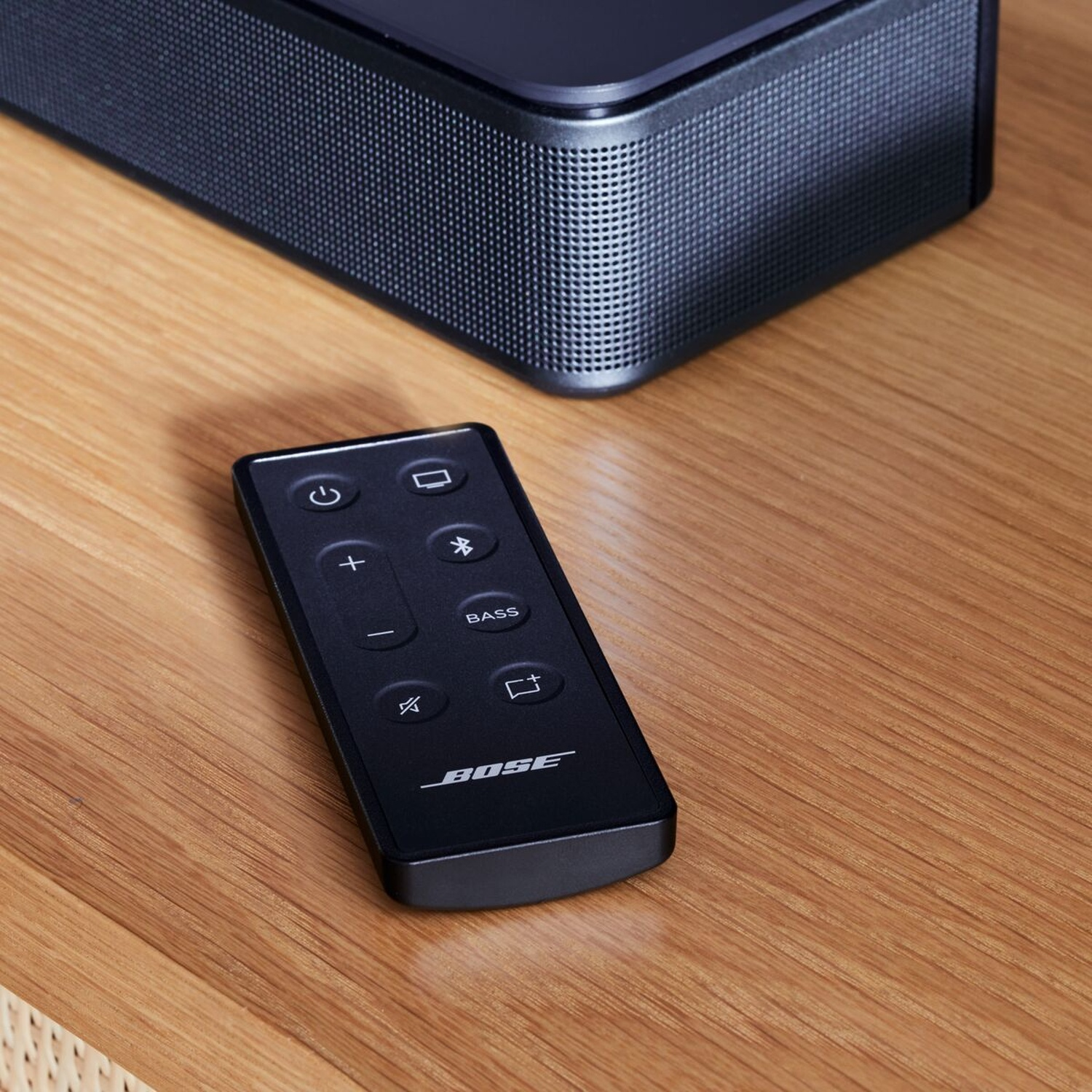Una soundbar Bose nera e un telecomando nero. Il telecomando è su una superficie in legno.