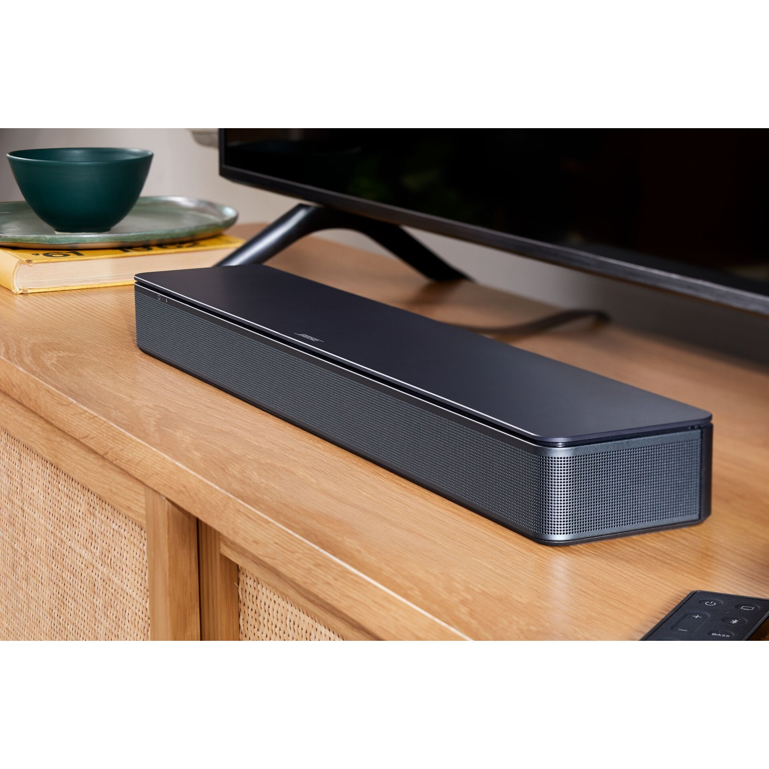 Una soundbar nera su un mobile in legno, con TV e telecomando. Sfondo scuro.