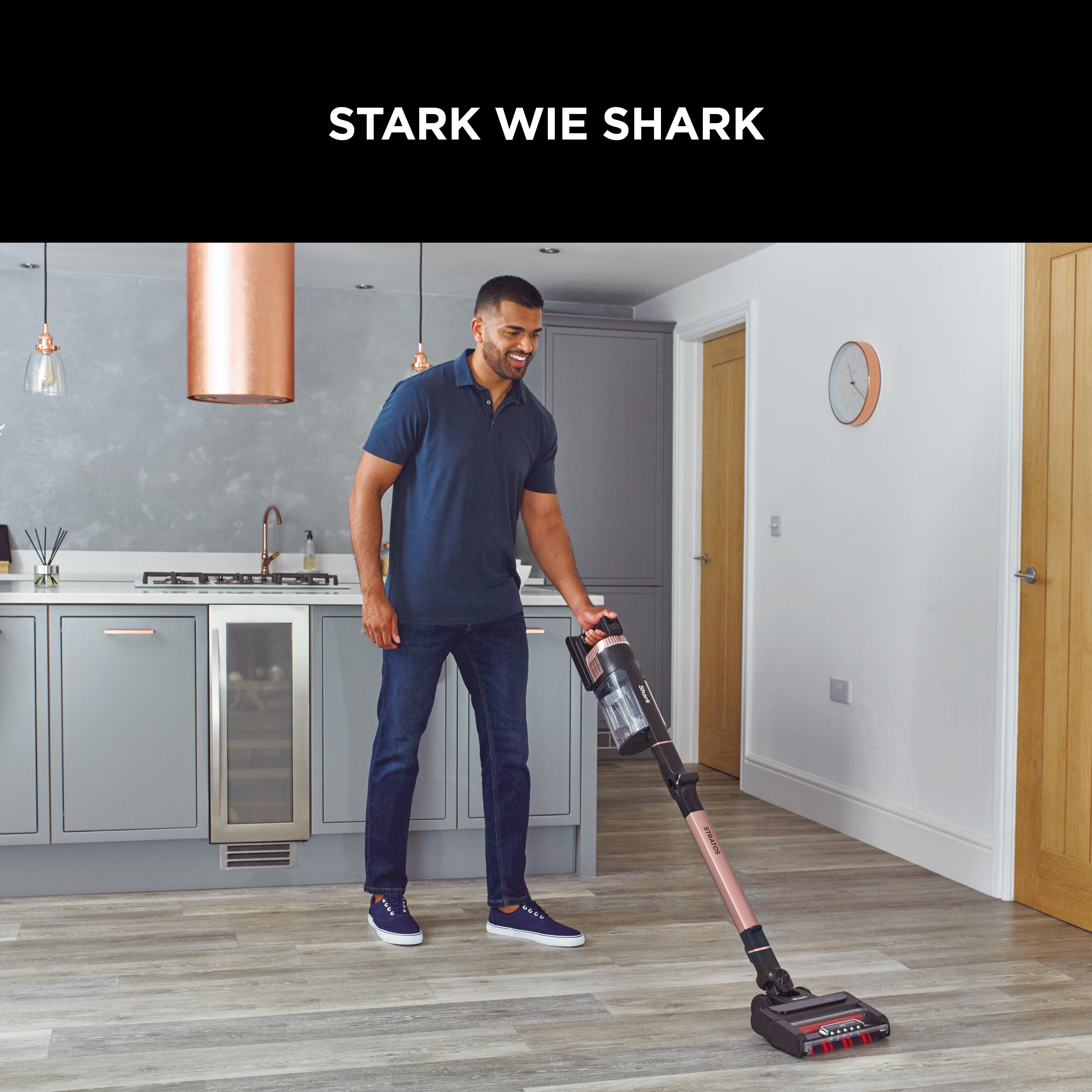 Ein Mann saugt in einer Küche mit einem roségoldenen Staubsauger den Boden.
