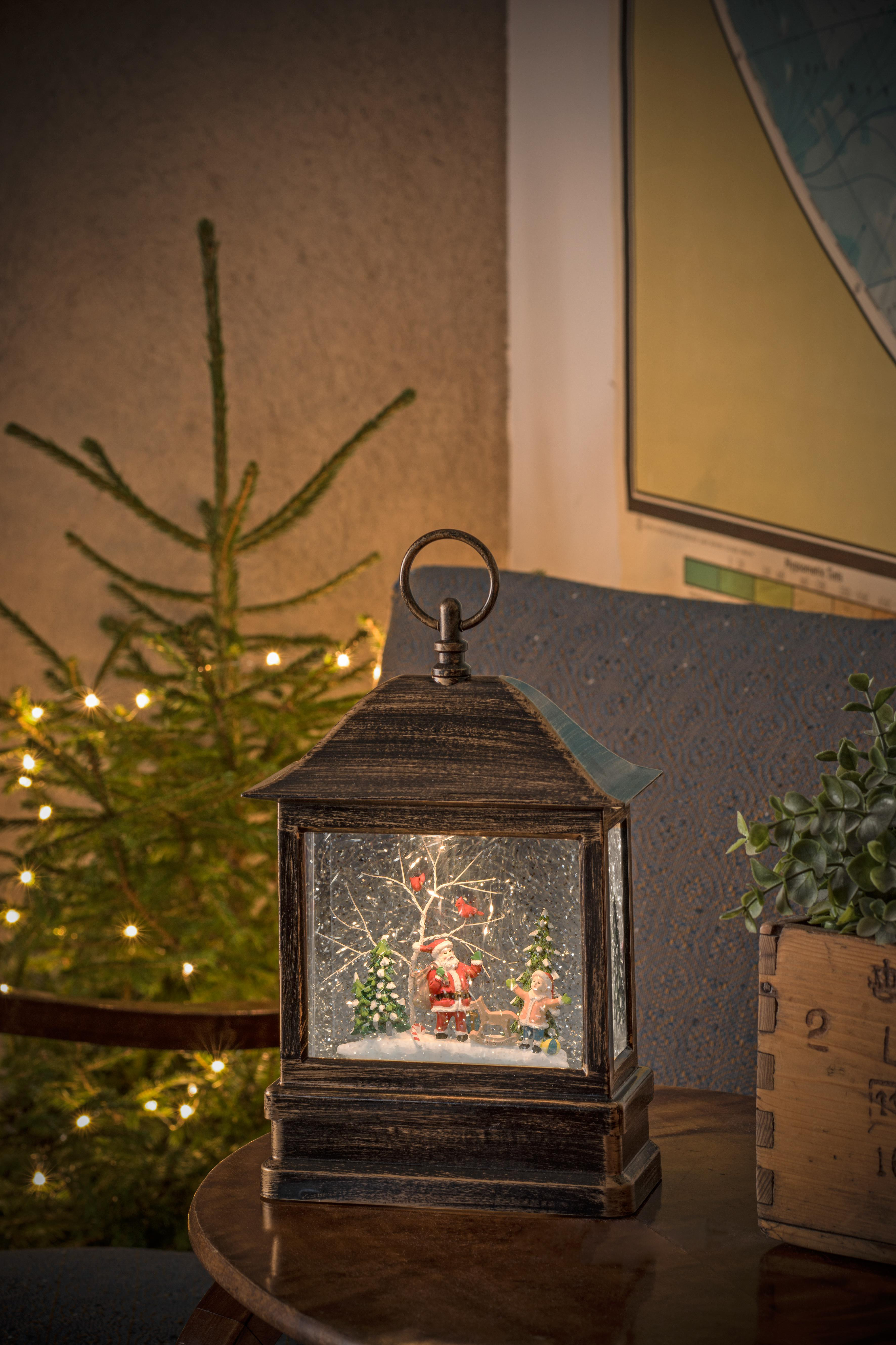 Schneekugel mit Weihnachtsmann und Kind in einer beleuchteten Laterne. Ein kleiner Weihnachtsbaum steht daneben.