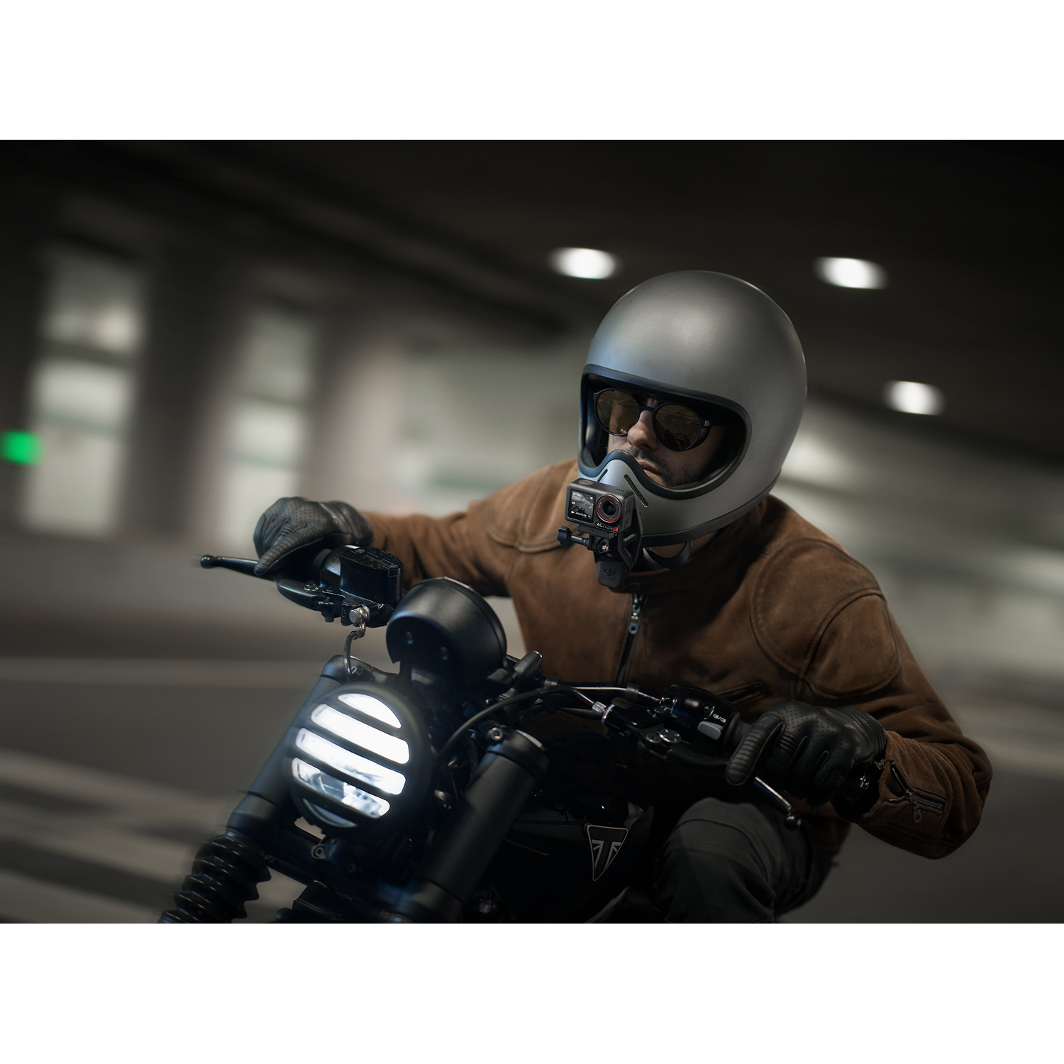 Uomo su moto, casco con telecamera. Moto nera, sfondo sfocato.