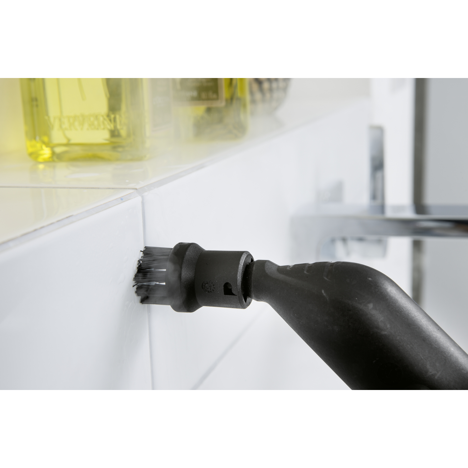 Steam cleaner nozzle cleaning white tile wall, close-up view.