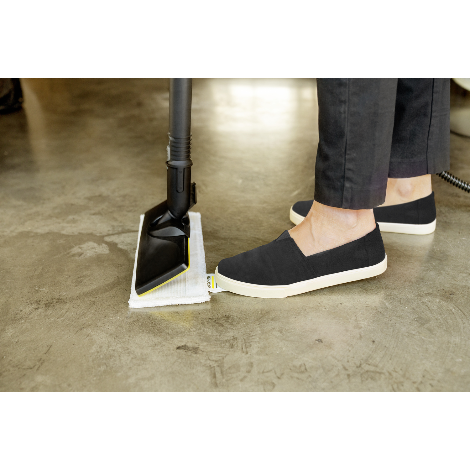 A person cleaning a floor with a black and yellow steam mop and black shoes.