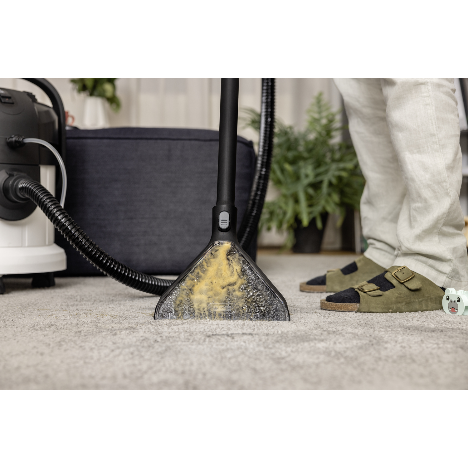 Carpet cleaner head on carpet, vacuum, and person's feet.