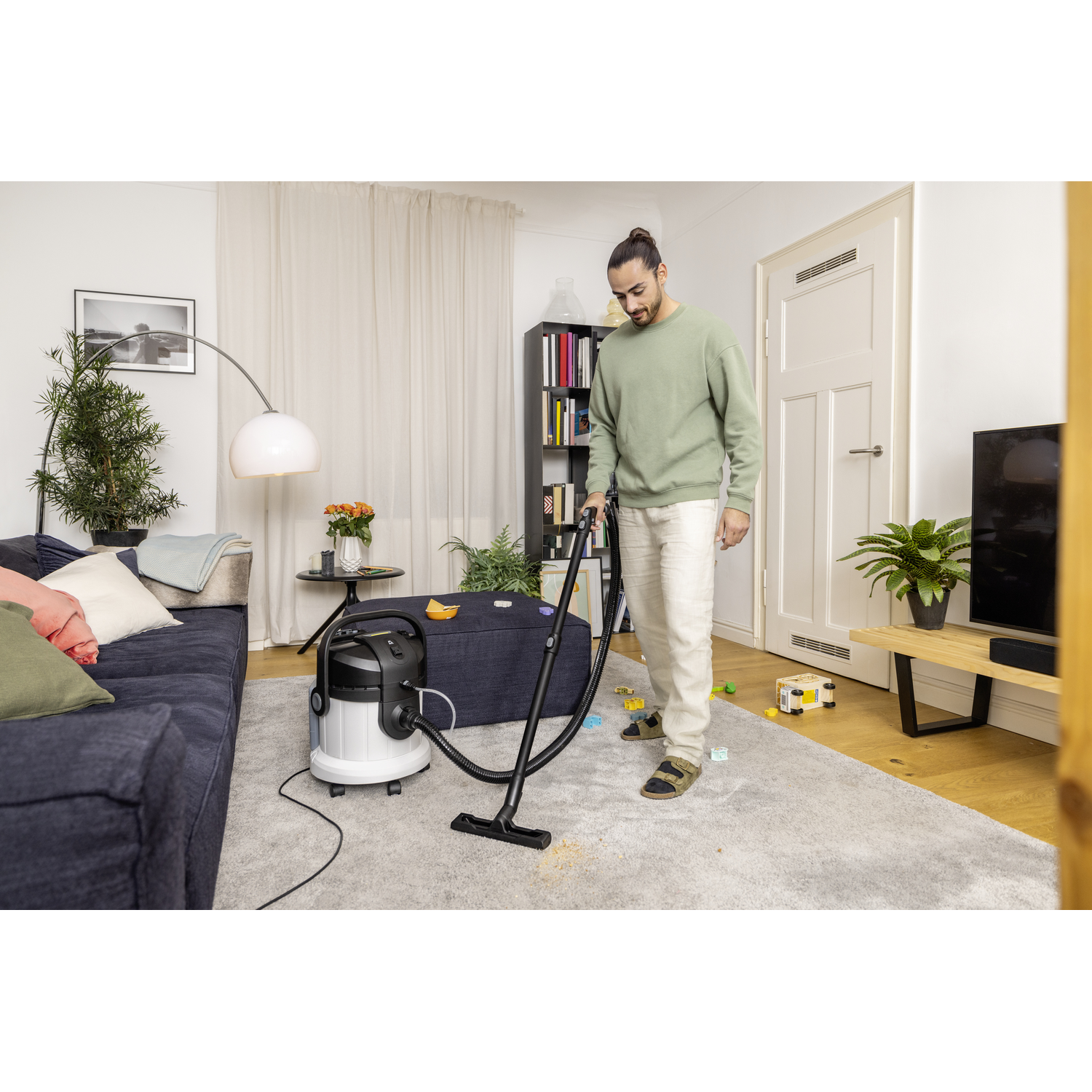 A man using a vacuum cleaner in a living room. The vacuum is white and black, and the room is tidy.