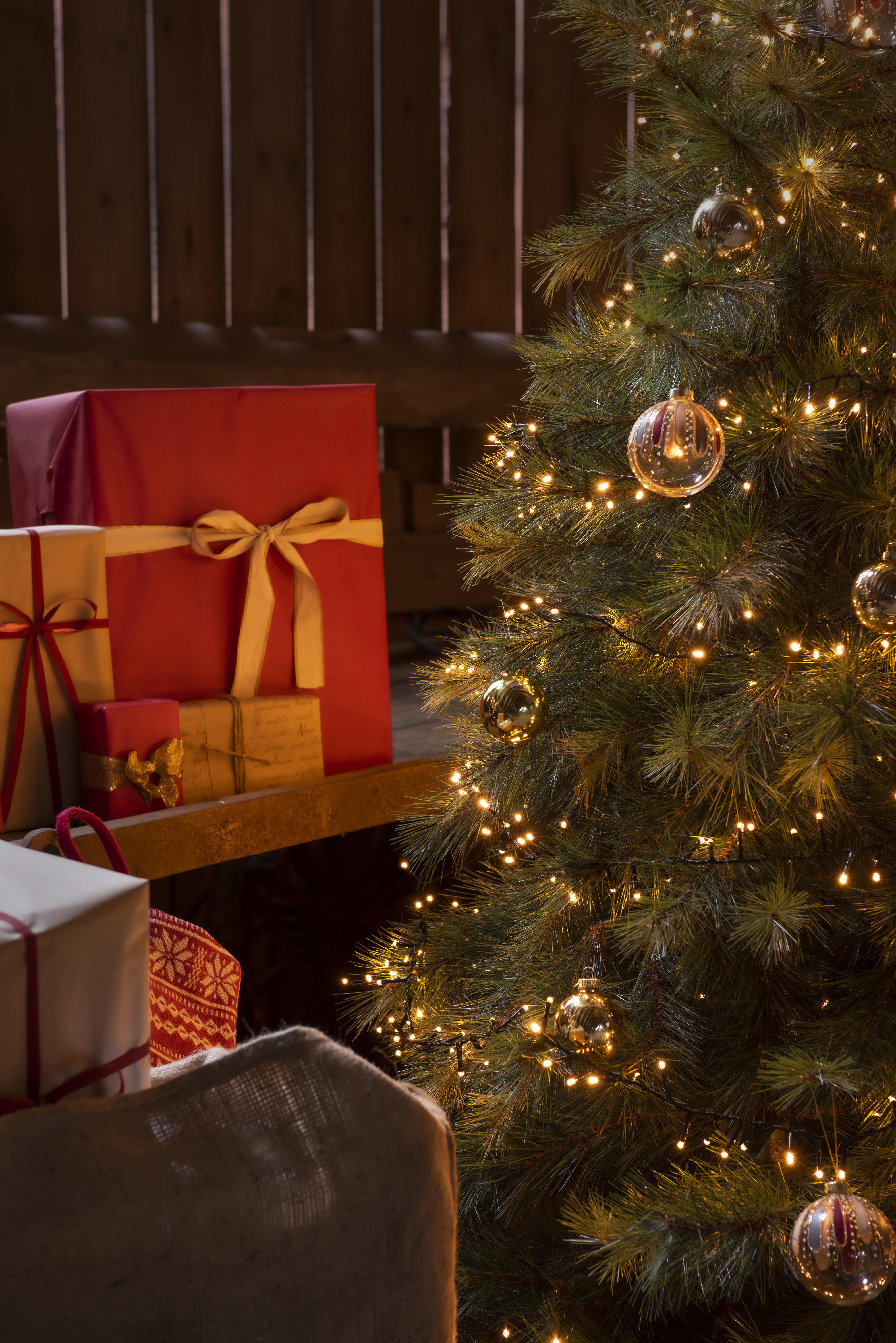 Weihnachtsbaum mit Lichtern und Schmuck. Geschenke in Rot, Braun und Weiß in der Nähe.