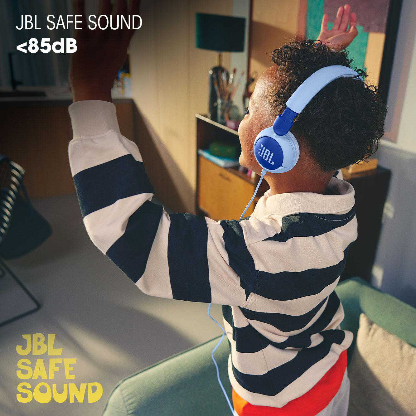 Ein Kind mit blau-weißen Kopfhörern, das die Arme hebt, mit JBL Safe Sound Logo.