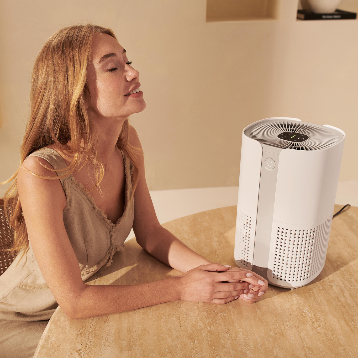 A woman and a white air purifier on a table in a softly lit room.
