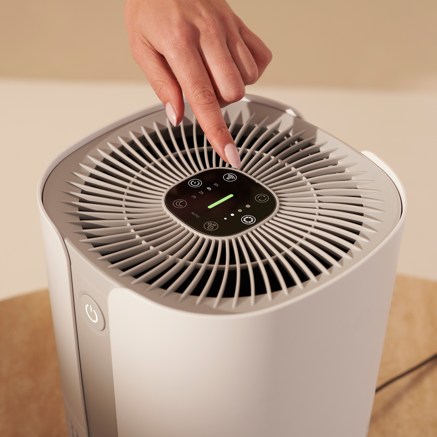 A hand pressing the touch control panel of a white air purifier.