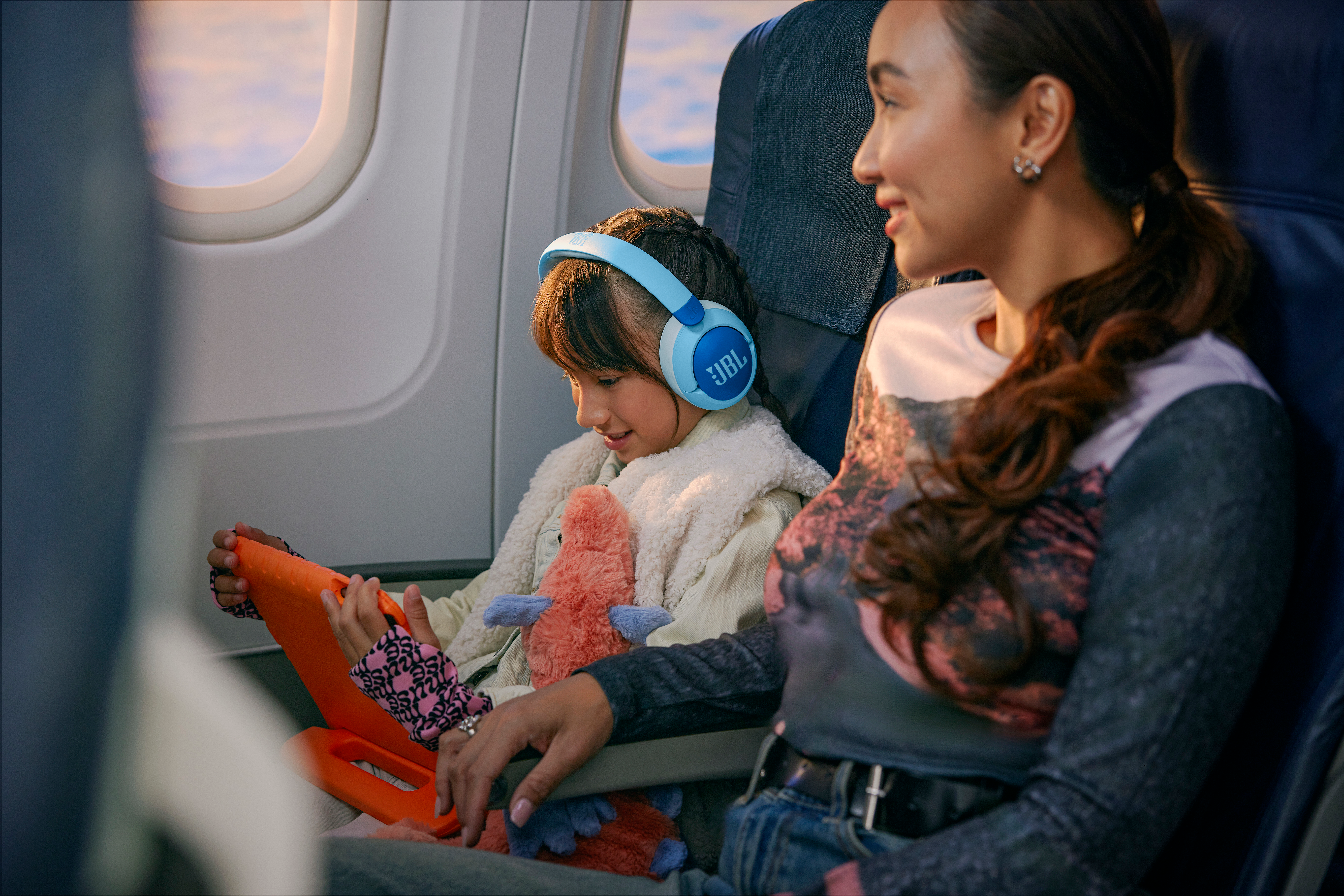 Ein Kind mit blauen JBL-Kopfhörern in einem Flugzeug. Eine Frau sitzt neben dem Kind.