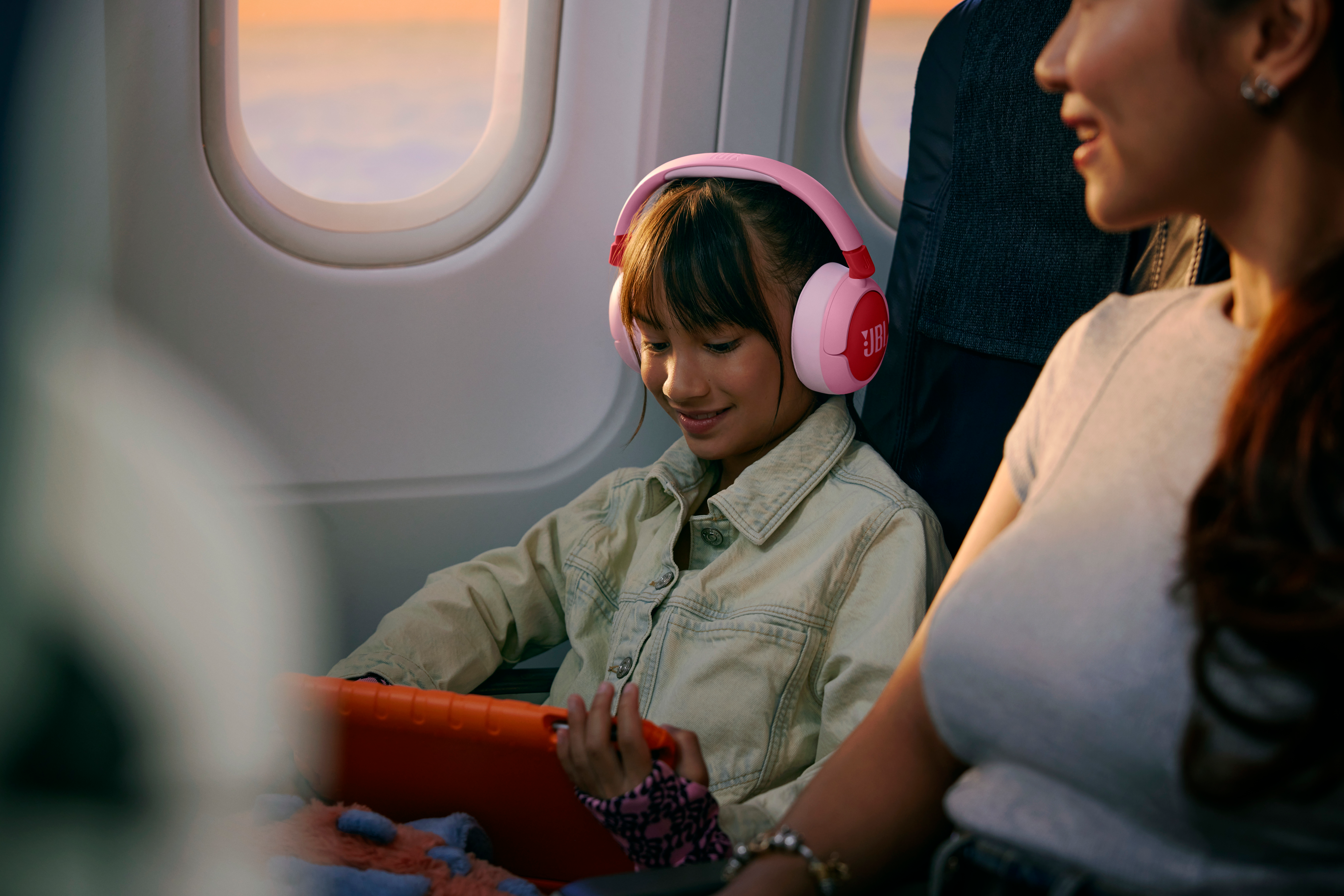 Ein Mädchen mit rosa Kopfhörern im Flugzeug, das auf ein Tablet schaut.