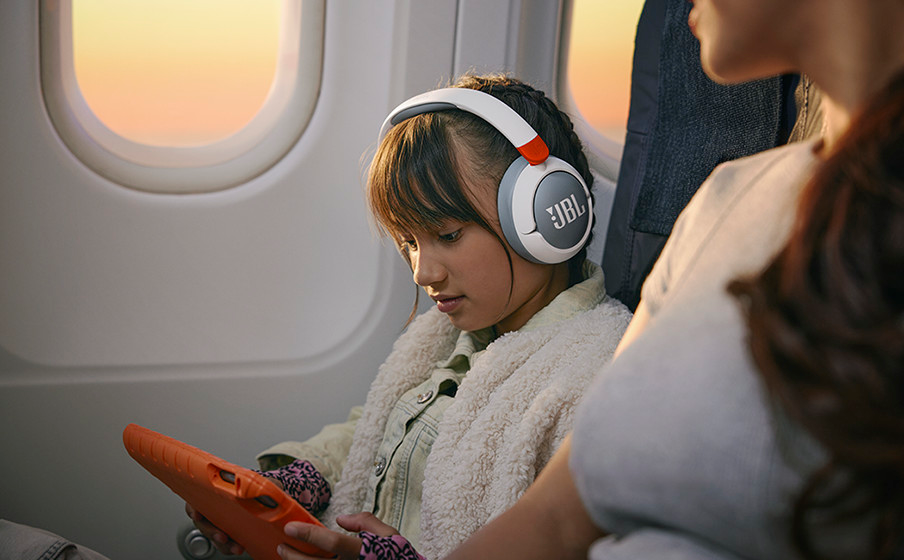 Ein junges Mädchen mit JBL-Kopfhörern im Flugzeug, das auf ein Tablet schaut.