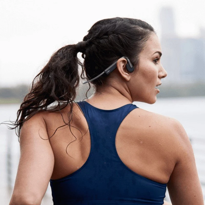 Una mujer con coleta corre mientras usa auriculares deportivos azules.