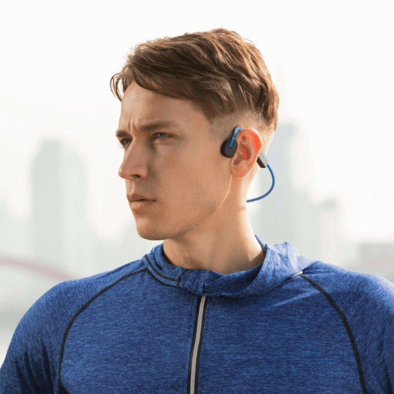 Hombre con auriculares azules para correr, mirando a la izquierda, fondo borroso.