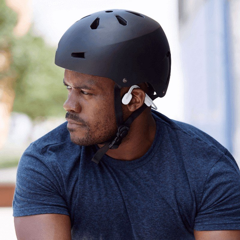 Un hombre con un casco negro y auriculares de conducción ósea blancos.