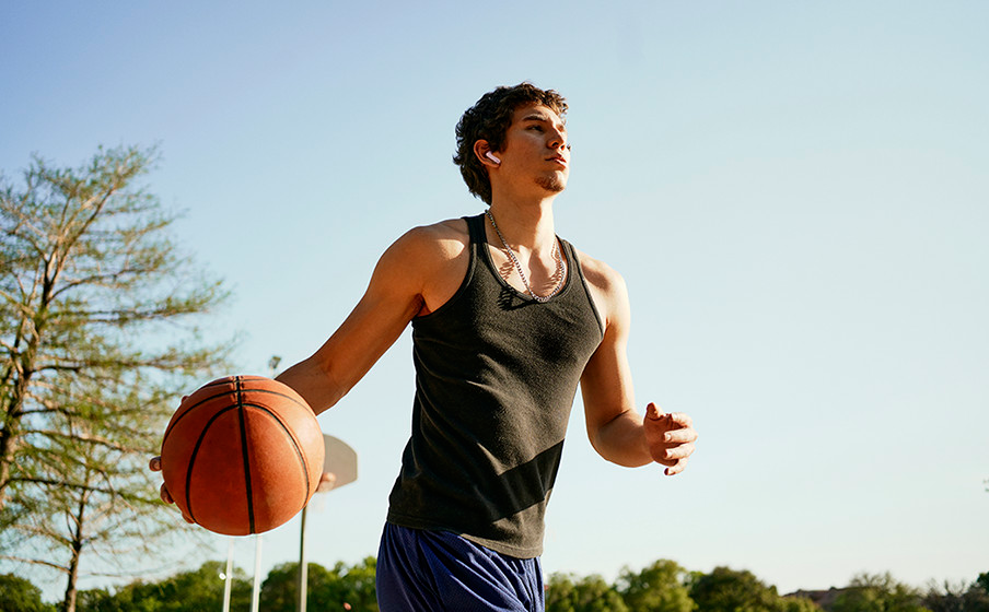 Mann dribbelt Basketball auf dem Platz, trägt Tanktop.