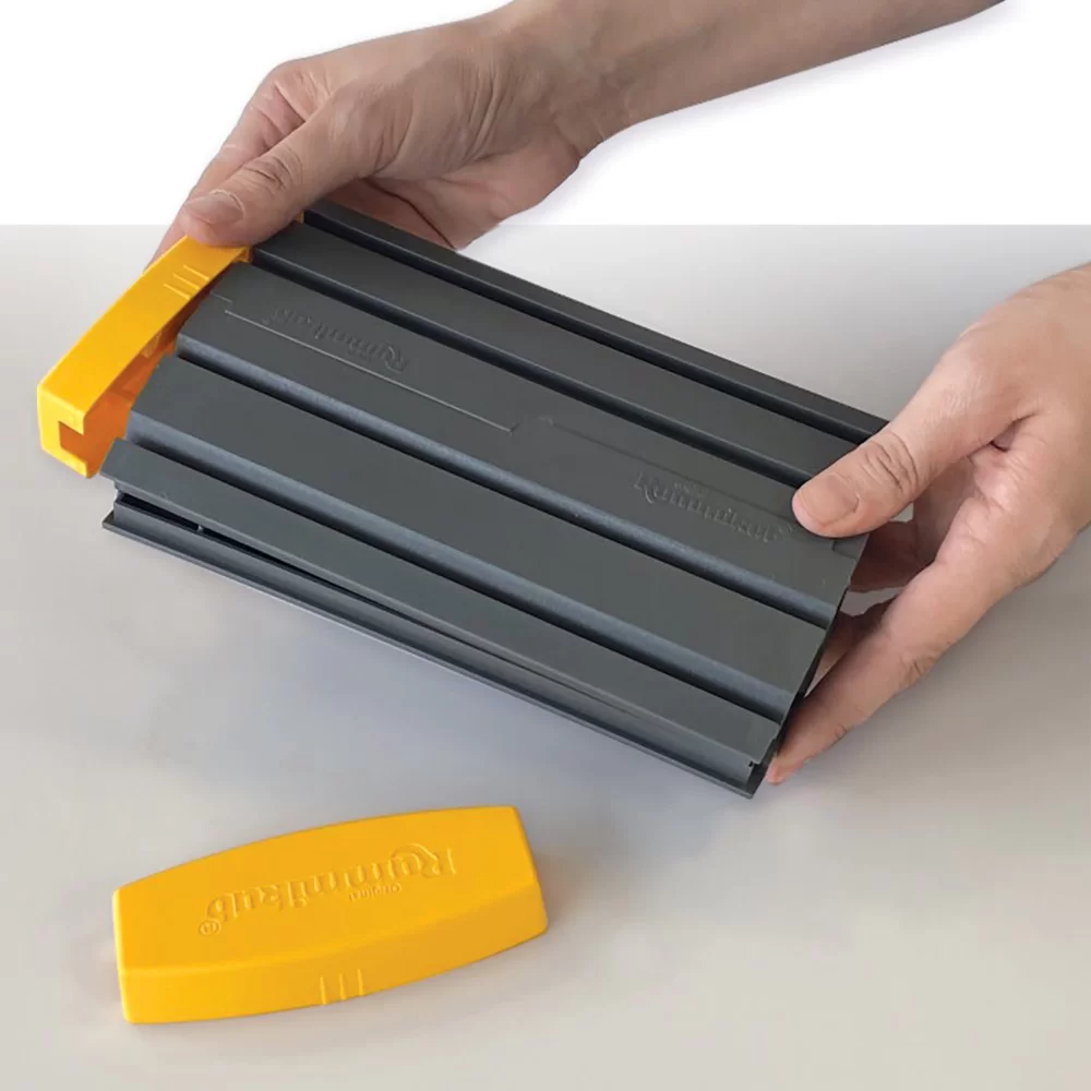 Ręce trzymające szare i żółte plastikowe narzędzie, z żółtym narzędziem w tle.