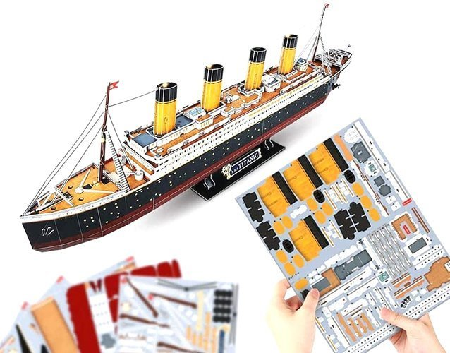 Model statku Titanic, obok części użytych do jego budowy. Ręce trzymają części.