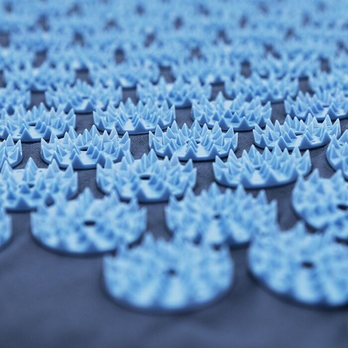Zbliżenie niebieskiej maty do akupresury z wieloma małymi, kolczastymi punktami. Mata leży na szarej powierzchni.