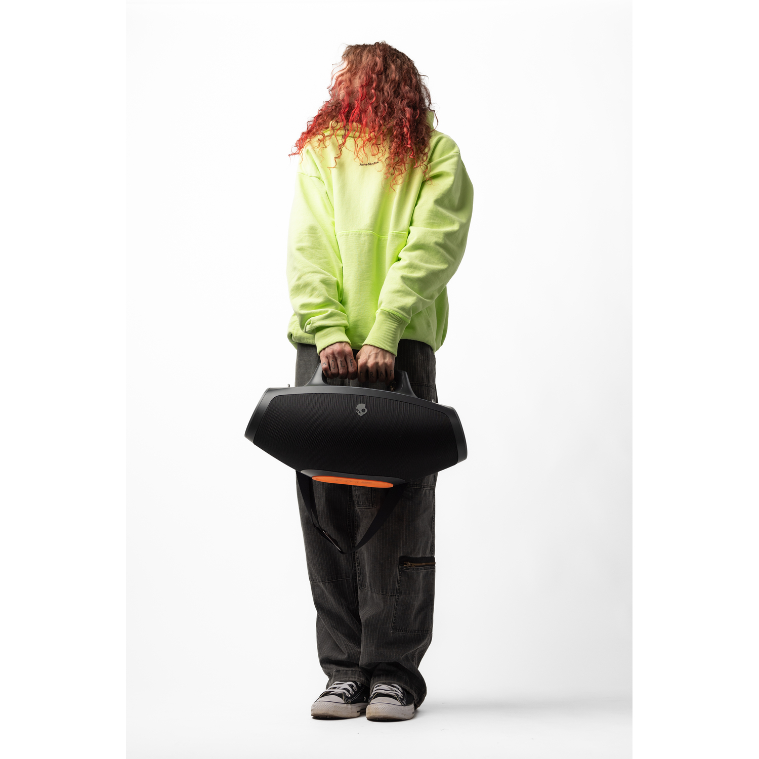 A person in a neon yellow hoodie holding a black boombox speaker against a white background.