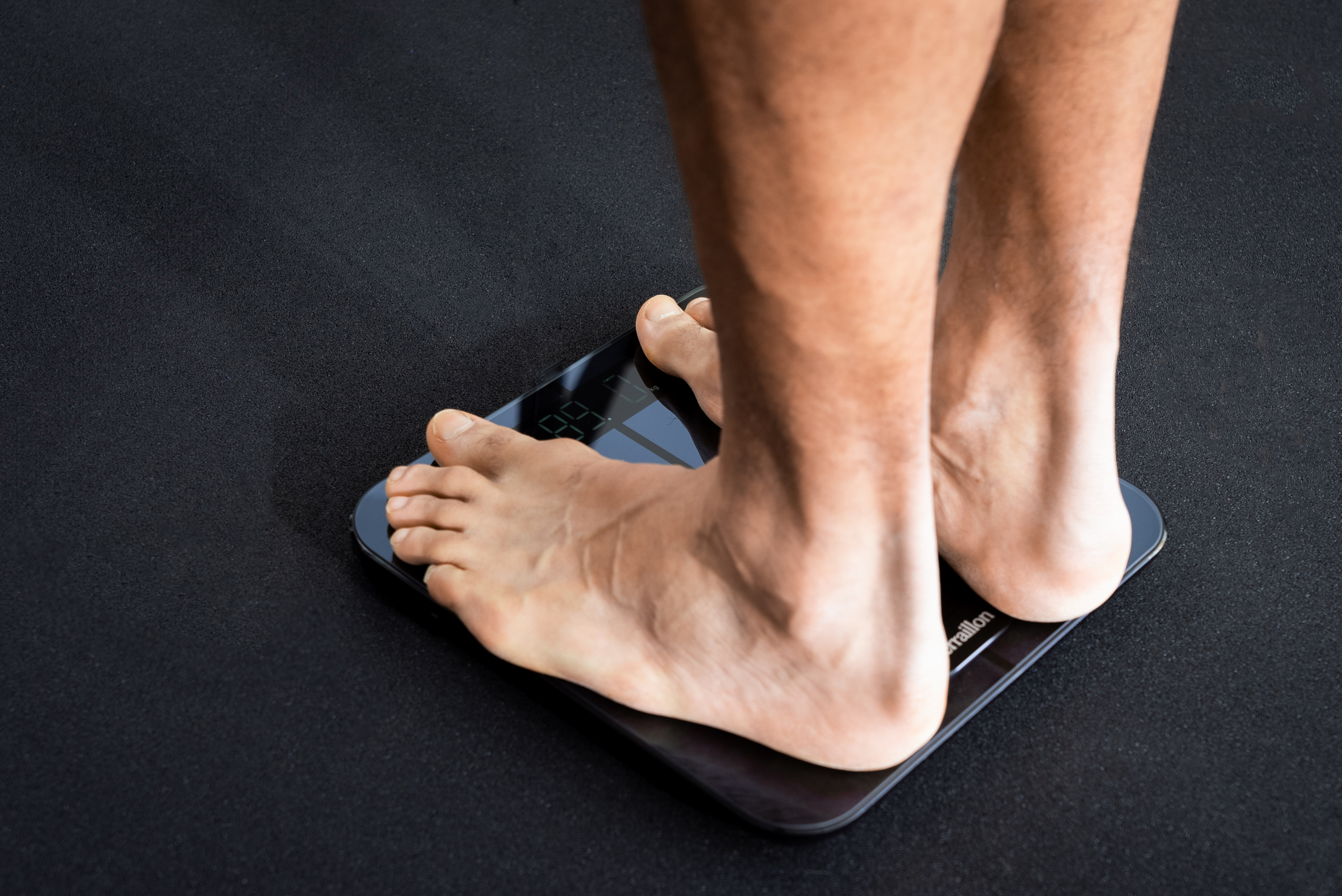 Piedi nudi su bilancia digitale, mostra il peso. Sfondo scuro.