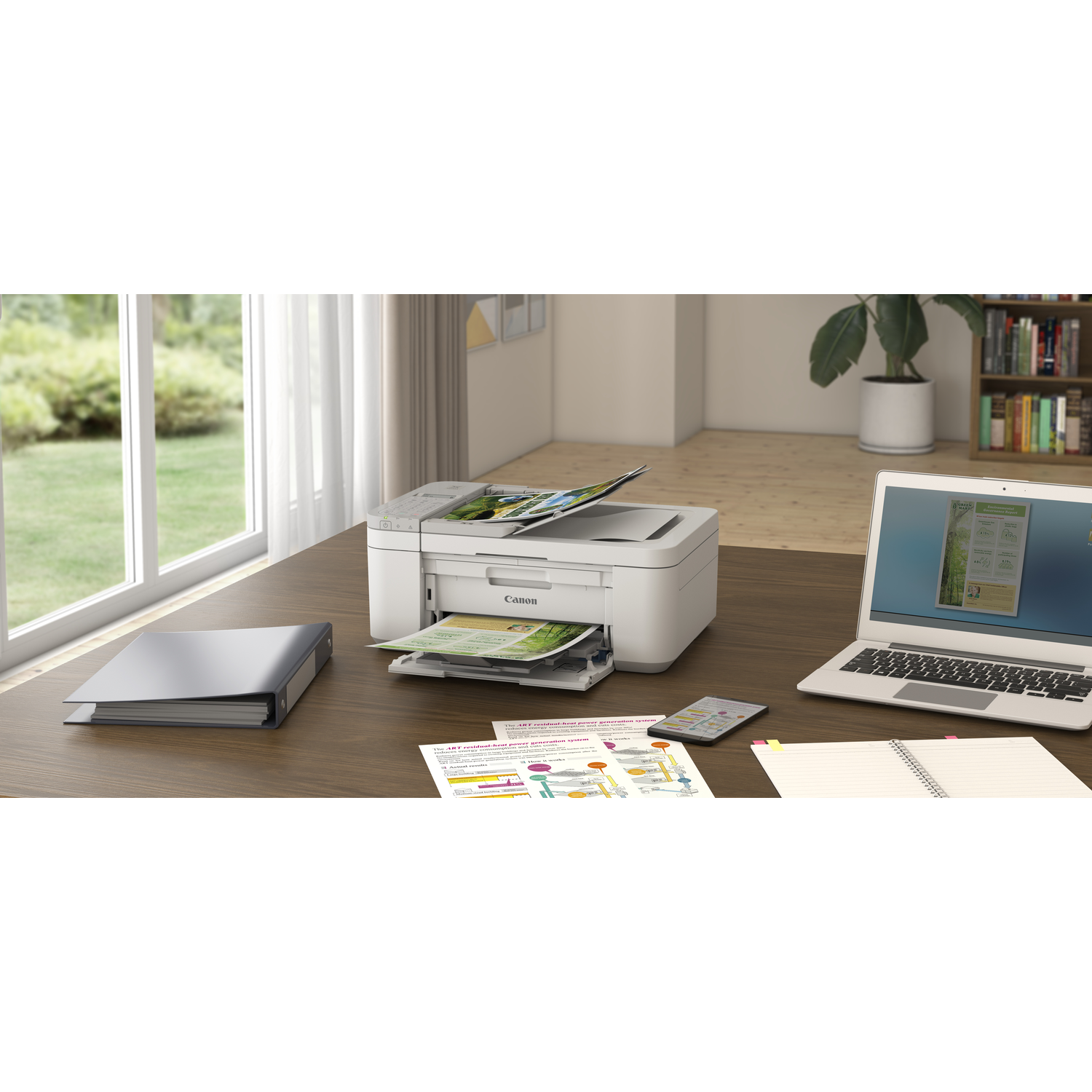 Canon printer on a desk, printing documents with a laptop, phone, and binder nearby.