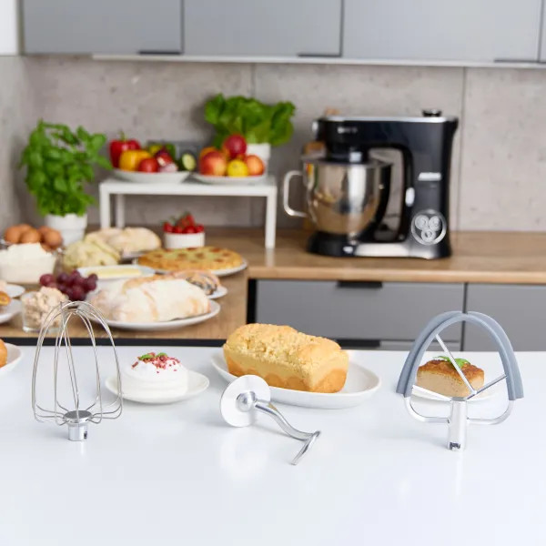 Kuchnia z chlebem, pizzą i mikserem z akcesoriami na stole.