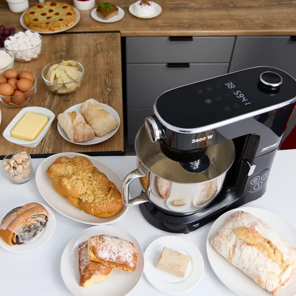 Czarny mikser kuchenny z chlebem i składnikami na stole.