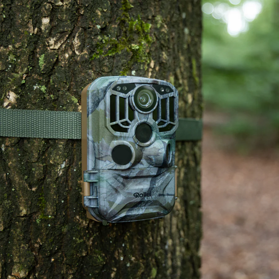 Une caméra de surveillance Rollei à motif camouflage, montée sur un arbre avec une sangle verte.