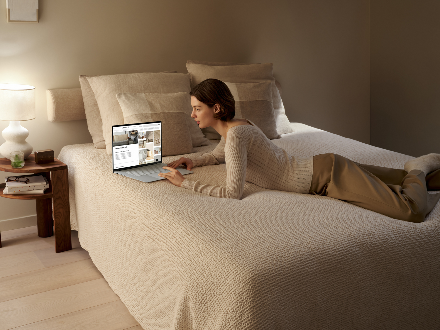 Mujer en cama usando portátil, ropa de cama beige.