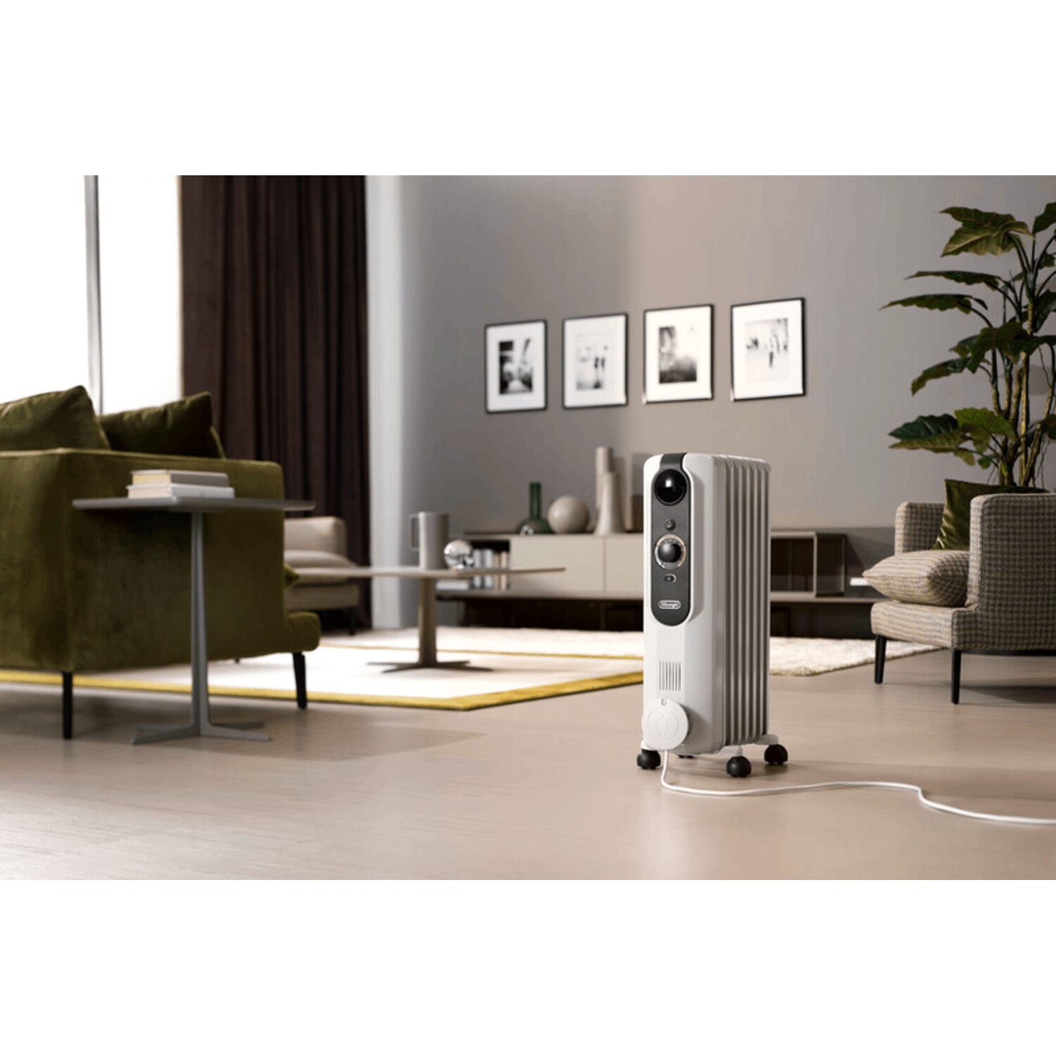 Witte olieradiator in woonkamer. Achtergrond: meubels, plant, raam.