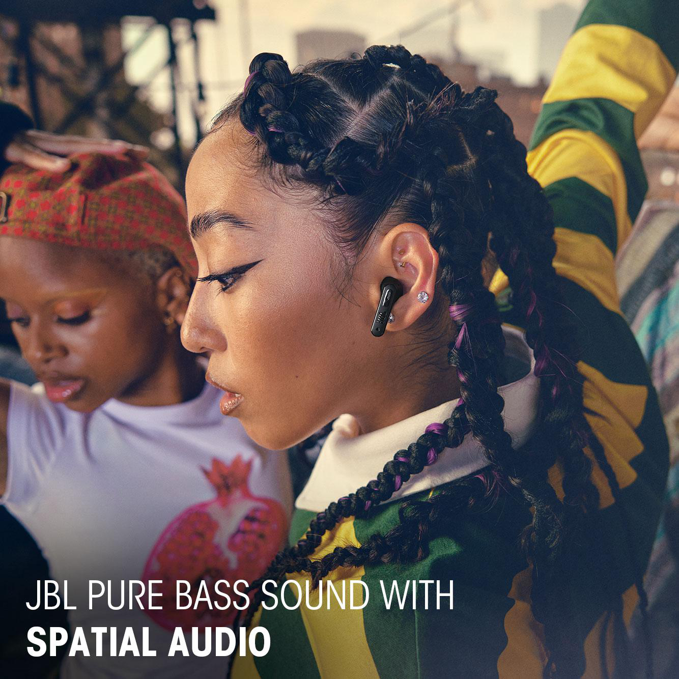 Eine Frau mit geflochtenen Haaren trägt schwarze Ohrhörer. Text unten lautet 'JBL PURE BASS SOUND WITH SPATIAL AUDIO'.