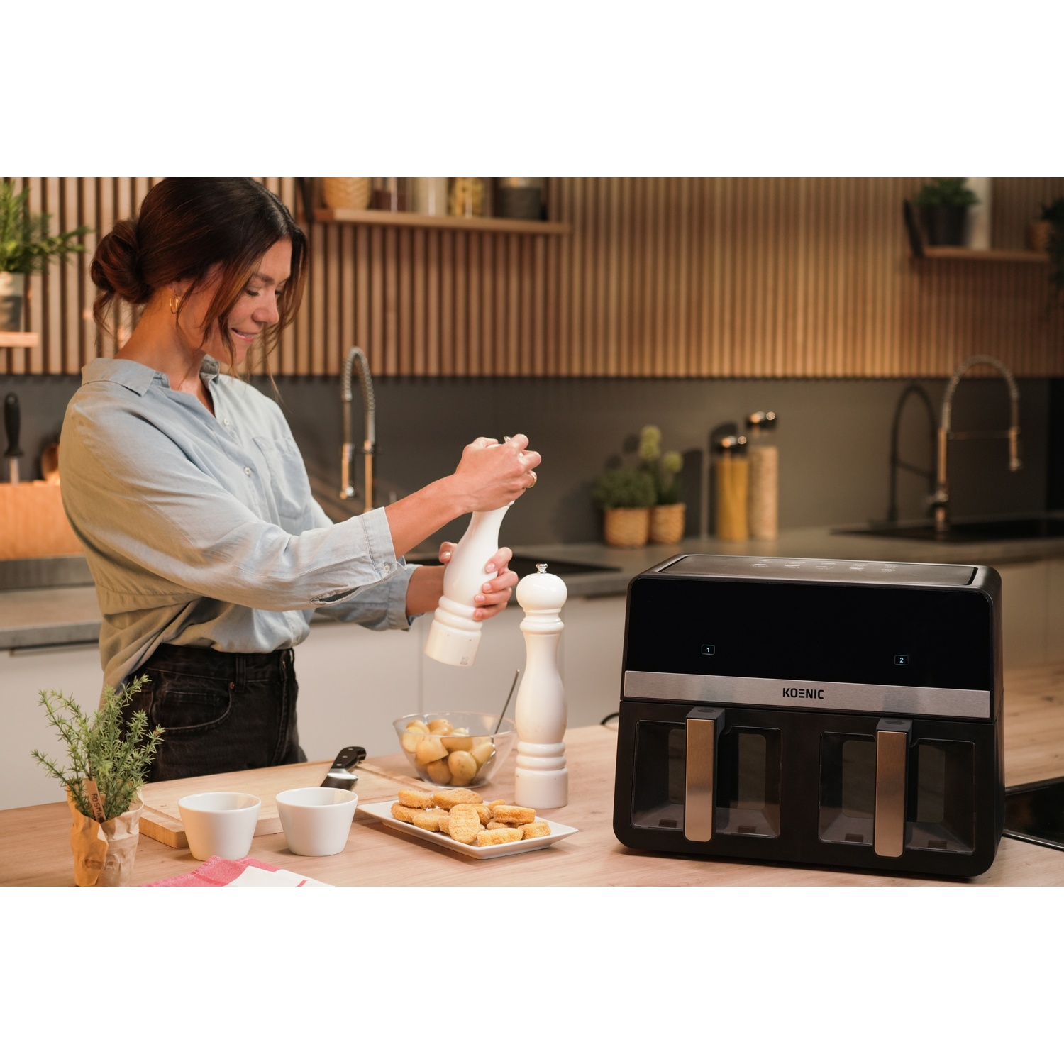 Una donna cucina con una friggitrice ad aria e saliere/pepiera su un bancone.