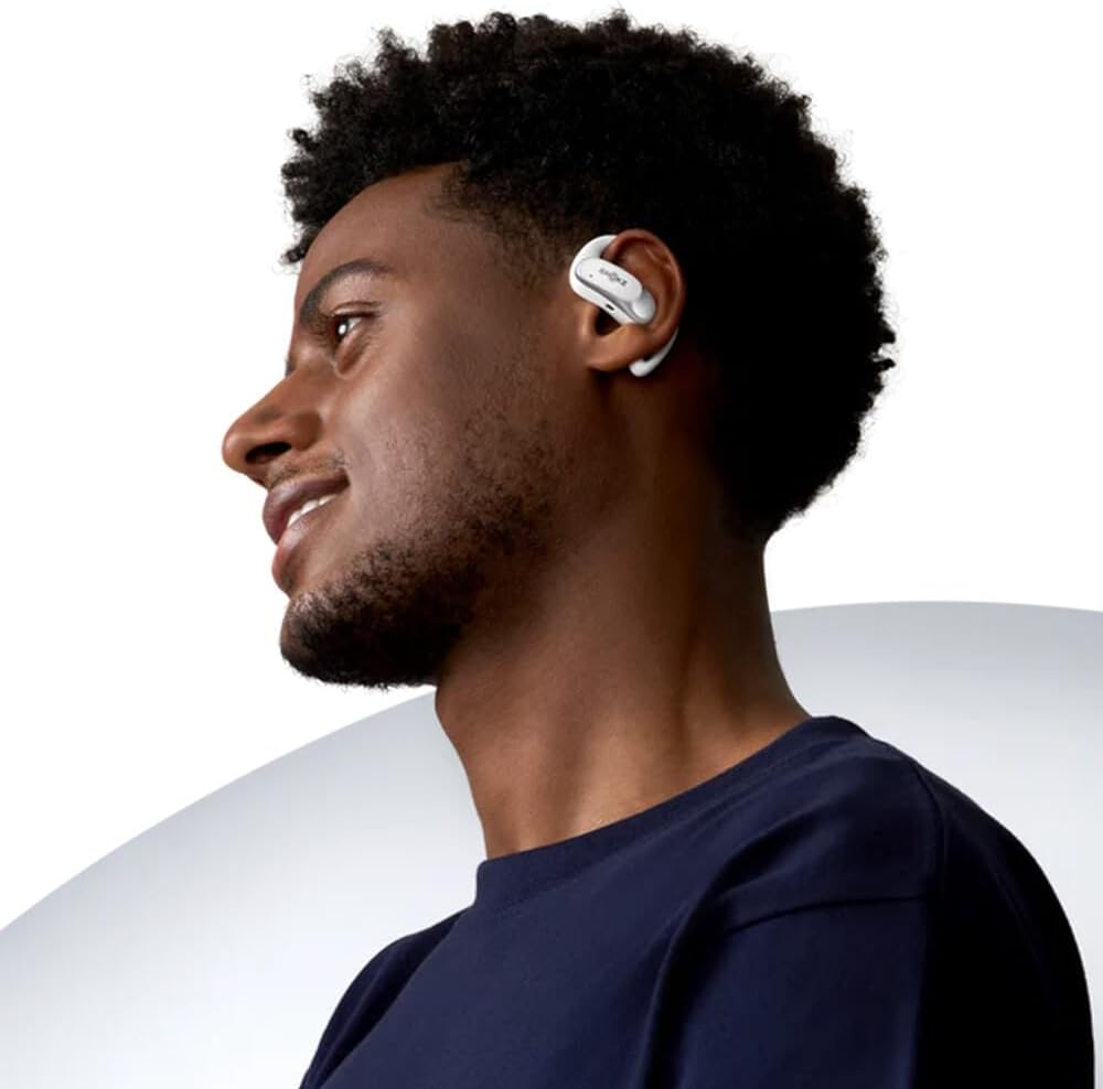 Joven con auriculares blancos. Está sonriendo y hay un fondo blanco detrás de él.