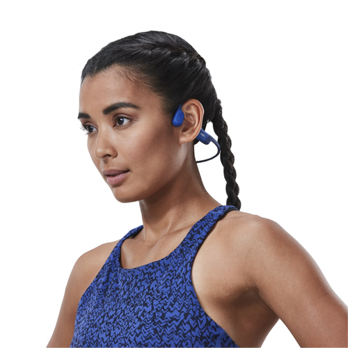 Mujer con auriculares azules. Mira hacia otro lado. Fondo blanco, plano del torso.