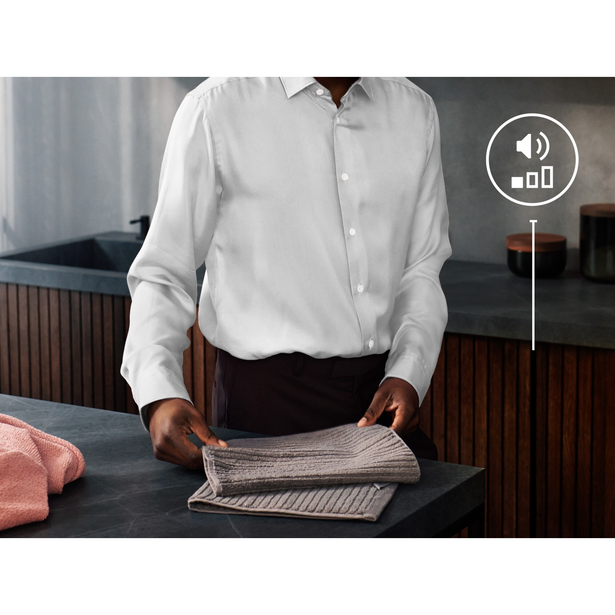 Una persona con camisa blanca y pantalón oscuro doblando toallas en una encimera. Ambiente de cocina.