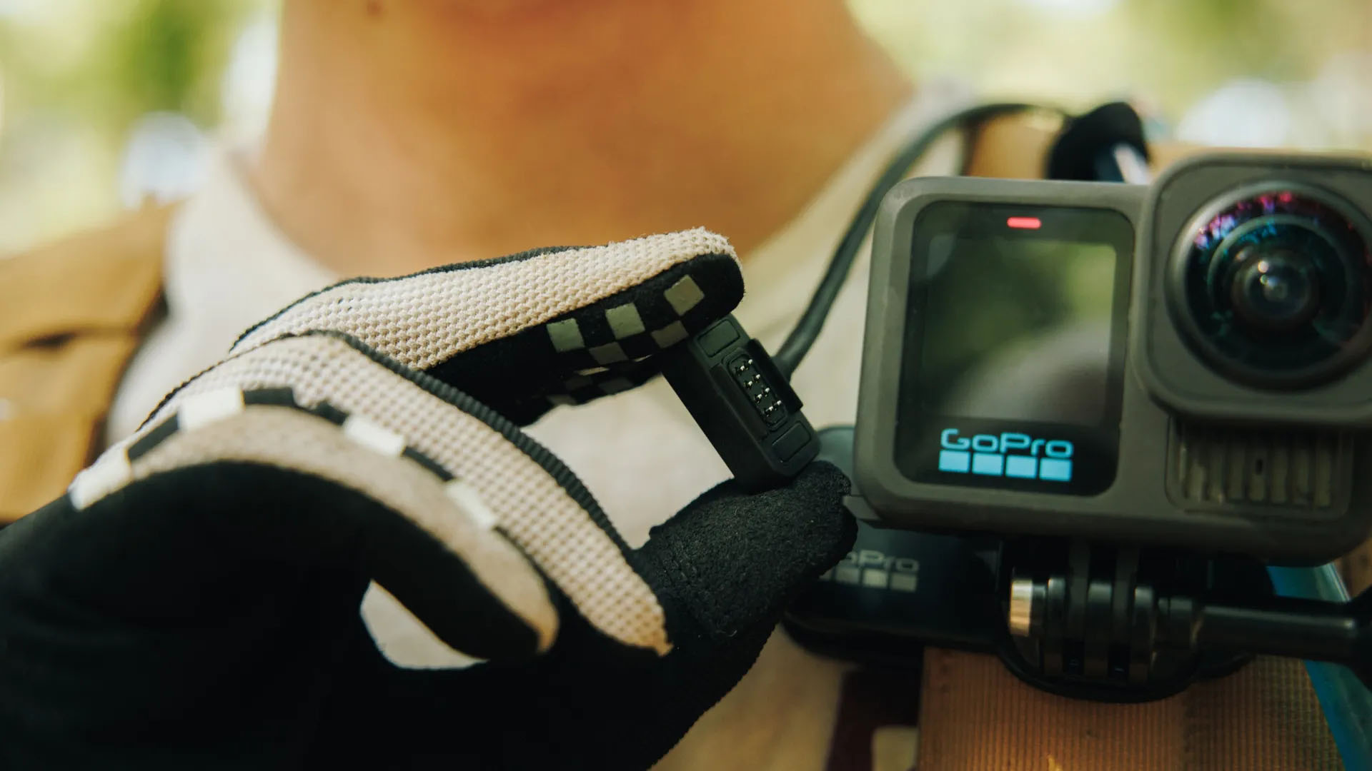 Göğüs kayışına takılı bir GoPro kameranın yanında siyah bir cihaz tutan bir kişi.