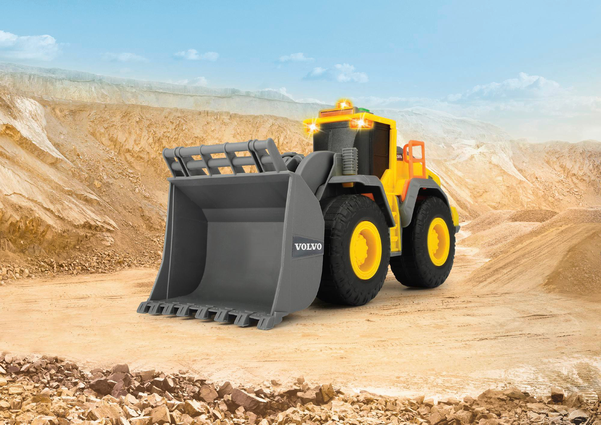 Gelb-grauer Volvo-Spielzeugbagger auf einer Baustelle, klarer Himmel.