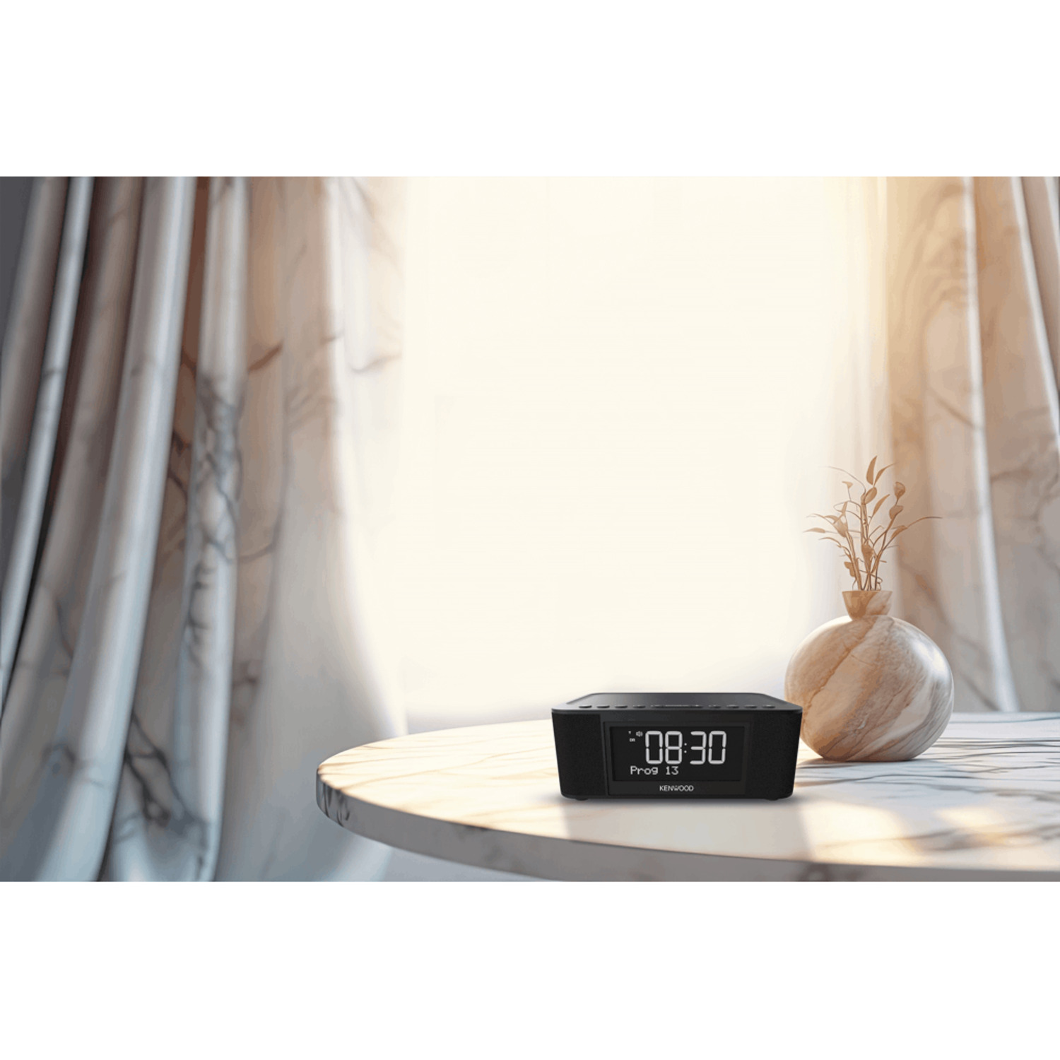 A black Kenwood clock radio on a table with a vase in front of a window.