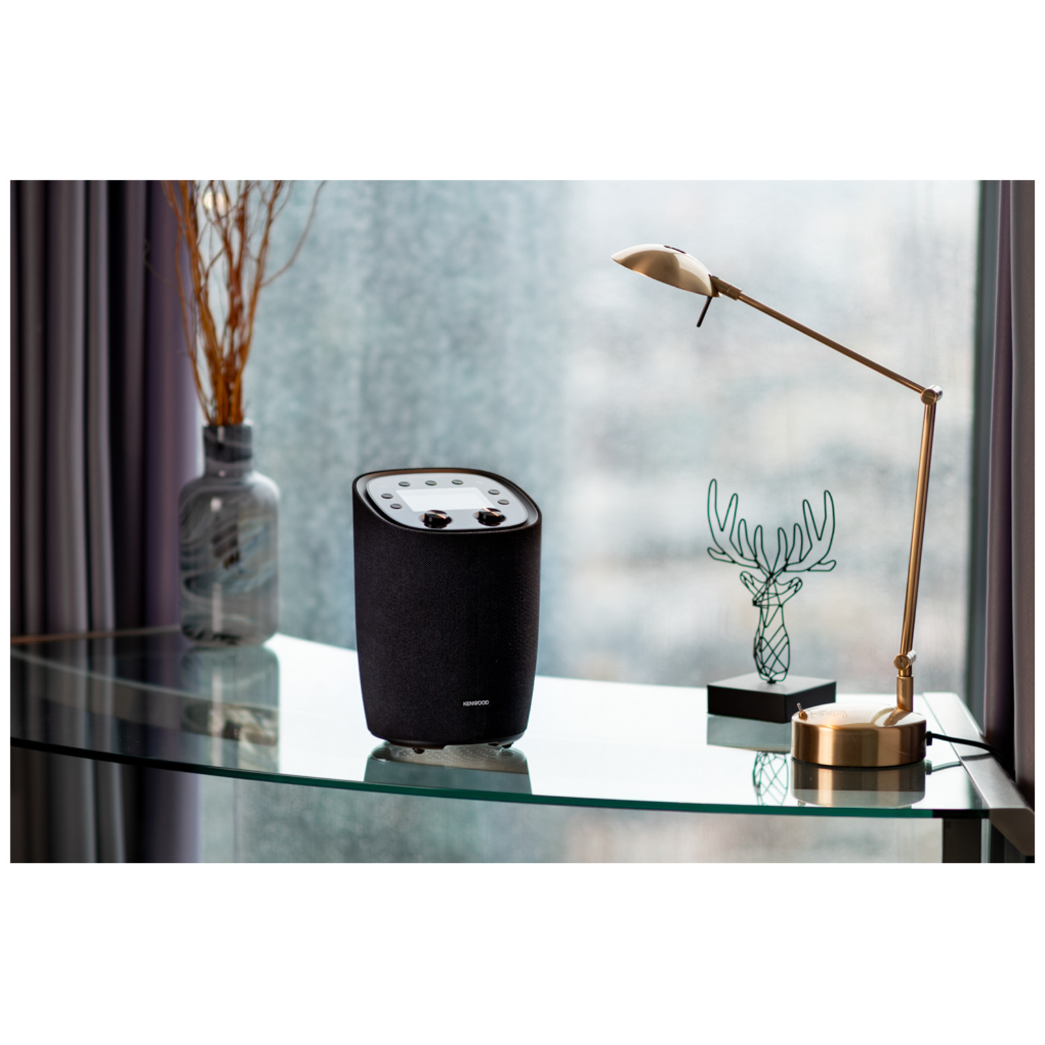 A decorated black speaker on a glass table. There are other items on the table.