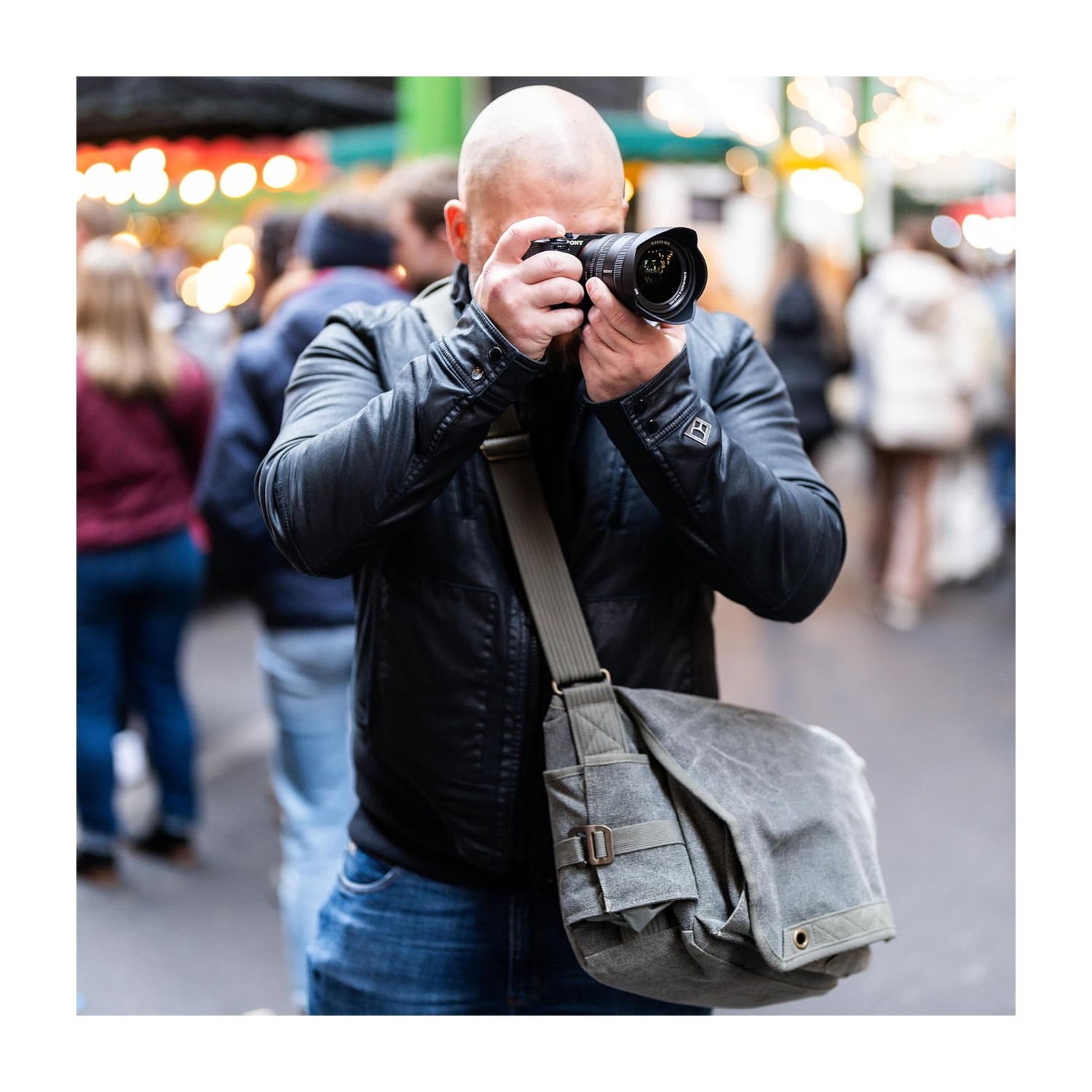 Un fotografo con una giacca nera con una fotocamera scatta foto su uno sfondo sfocato.