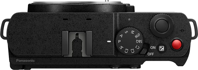 Vue de dessus d'un appareil photo Panasonic noir. Il comporte des molettes, des boutons, une griffe porte-flash et un bouton rouge d'enregistrement. L'appareil est texturé.
